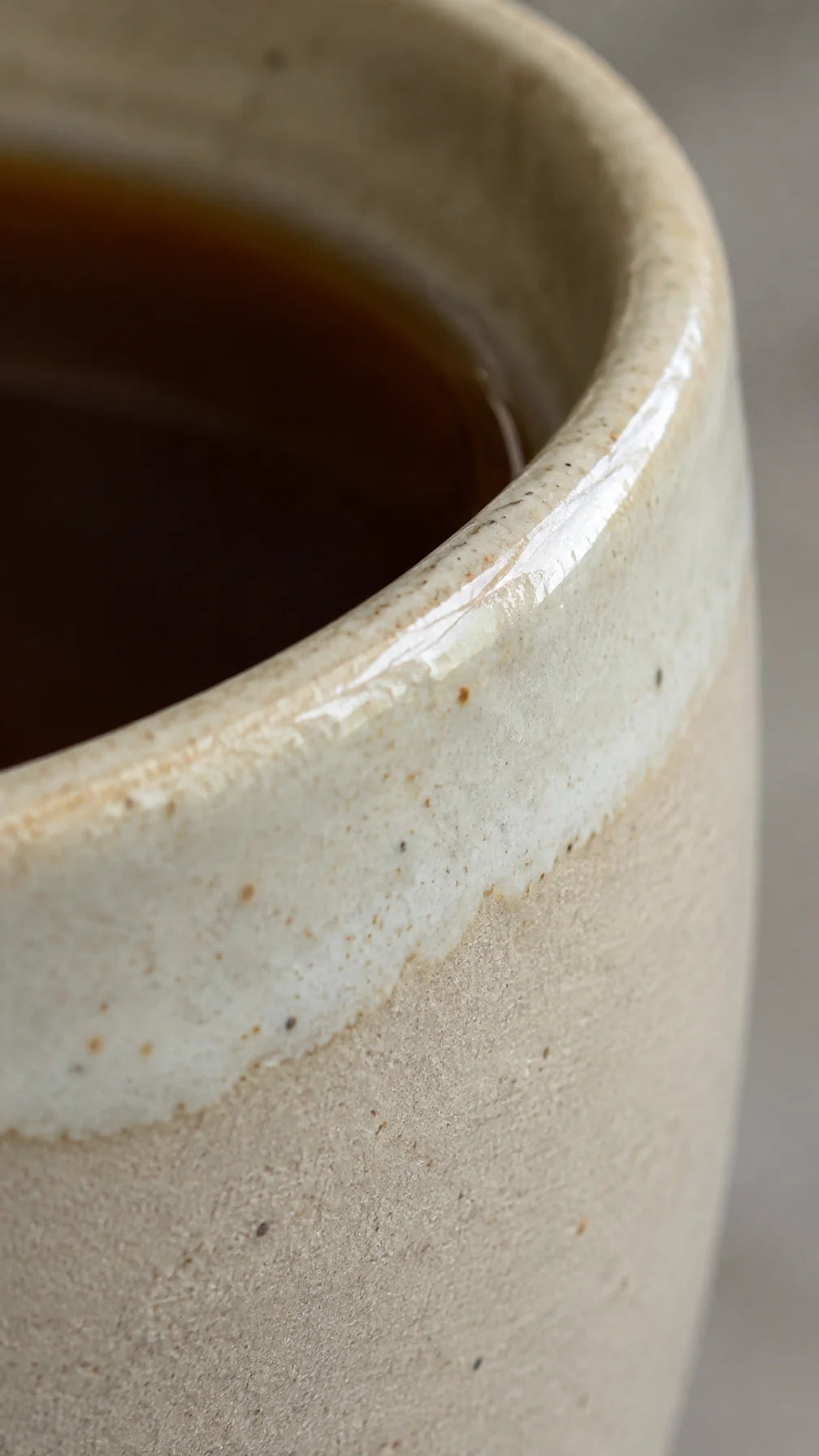 An extreme close photograph of the cream ceramic cup’s rim and glaze, showing a fine uneven glaze tr
